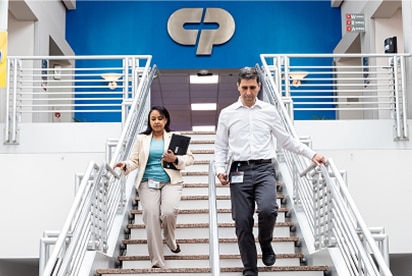 Mitarbeitende von Colgate-Palmolive, die eine Treppe hinuntergehen, mit einem Colgate-Palmolive-Logo hinter ihnen auf einer blauen Wand.