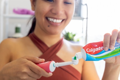 Eine lächelnde Frau, die im Badezimmer Colgate-Zahnpasta auf eine Zahnbürste gibt.