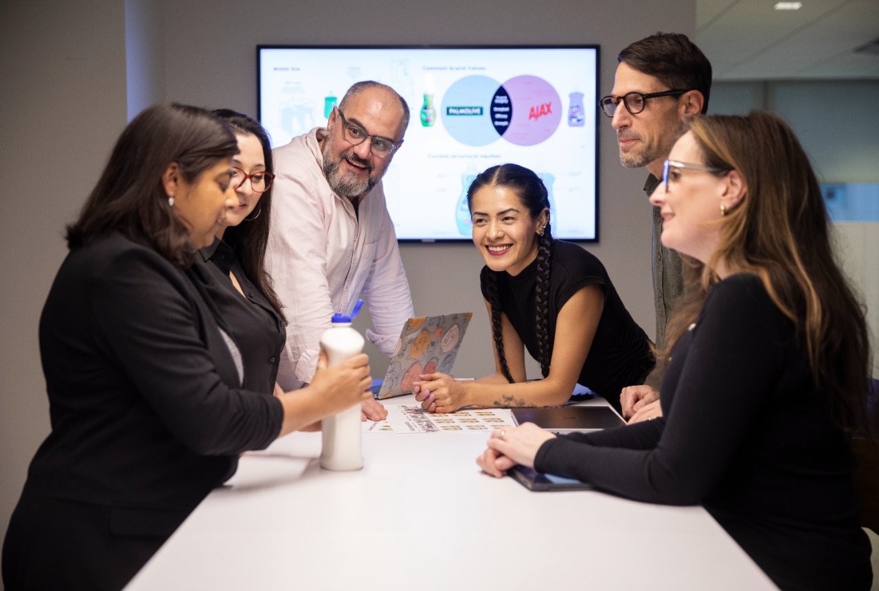 Six employés de Colgate-Palmolive dans une salle de réunion, en train de discuter d'un concept de produit, avec une diapositive de présentation projetée sur un écran derrière eux.