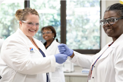 Deux scientifiques vêtus de blouses blanches et de gants sourient et se serrent la main dans un laboratoire.
